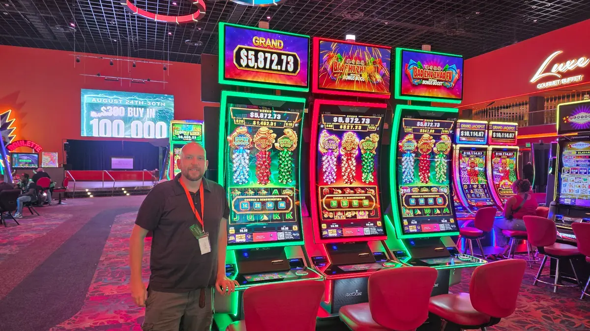 Wojtek beside three Bao Zhu Zhao Fu Bonus Boost slot machines at The Casino @ Dania Beach.