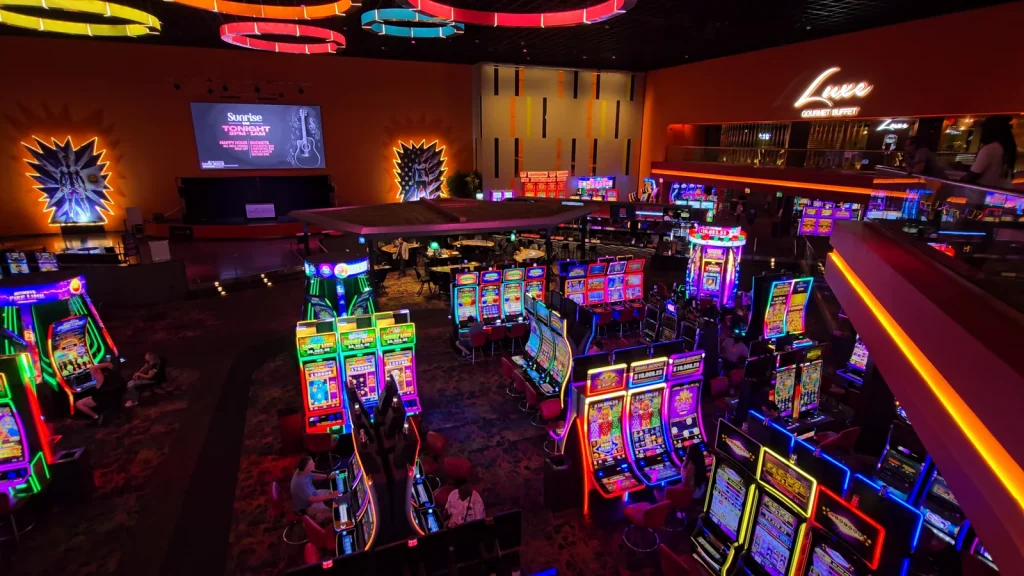 Casino floor view showing slot machines, the stage area, and Luxe Gourmet Buffet at The Casino @ Dania Beach.