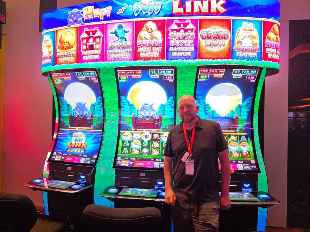 Wojtek in front of three Huff N’ Puff Link slot machines at The Casino @ Dania Beach.