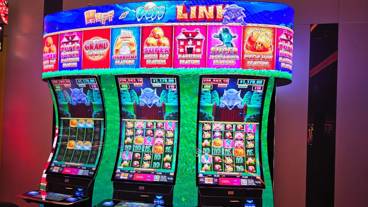 Three Huff N’ Puff Link slot machines beneath a shared feature display at The Casino @ Dania Beach.